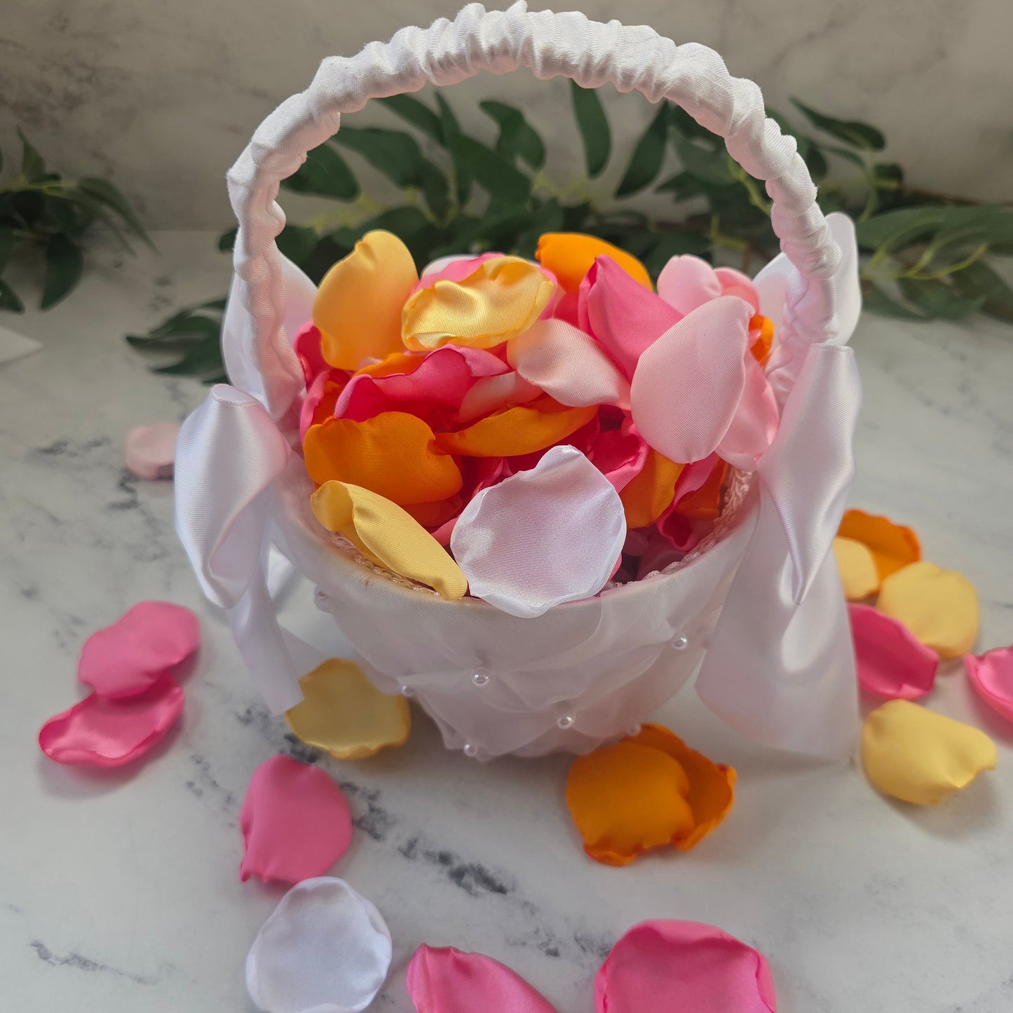 Orange, pink, white and yellow rose petals showcased in a white flower girl basket. perfect for wedding aisle decor, flower girl baskets, tablescapes, memory table accents. Sunset wedding decor , enchance your whimsical, boho, rustic western wedding ideas 