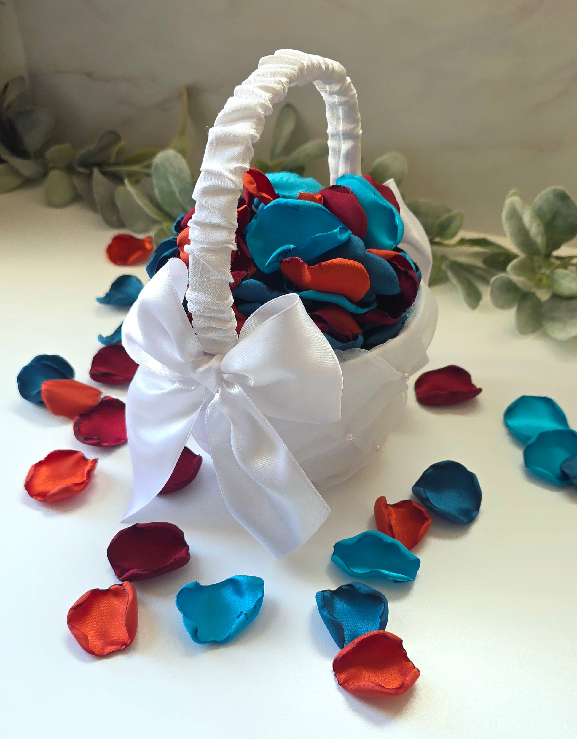 A mix of  burgundy, burnt orange, dark and light teal rose petals in white basket for flower girl tossing, aisle decor or tablescape  confetti scatter. Ideas for future brides planning a jewel toned wedding ceremony or fall bridal shower event.
