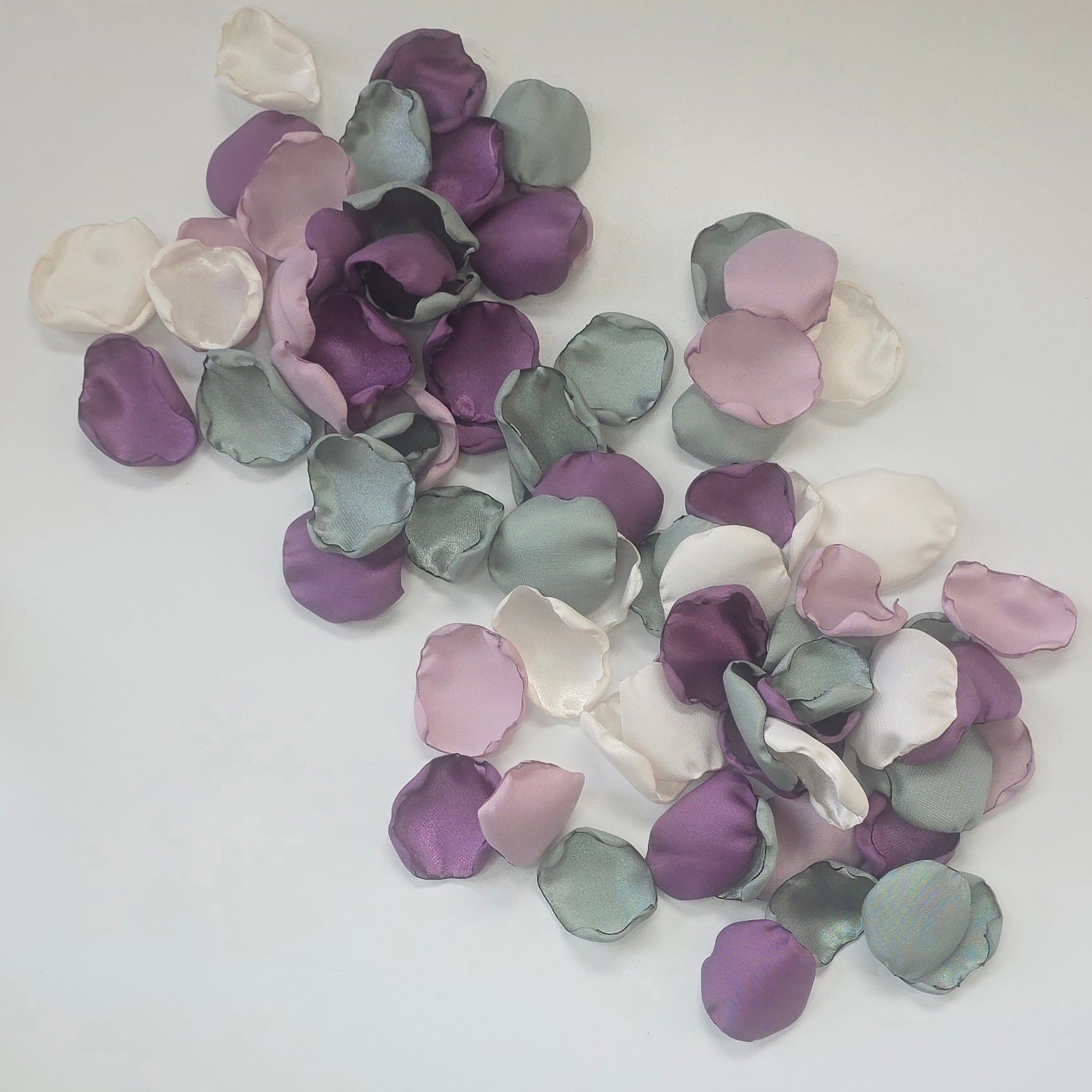 A mix of different shades of purple and sage green rose petals in Ivory flower girl basket. Includes Wisteria, Dusk Purple, Ivory and dusty sage rose petals for flower girl toss, aisle decor, photo flatlays, table scatter. Perfect for future brides planning a classic wedding or Love in Bloom or Whimsical bridal shower event ideas.