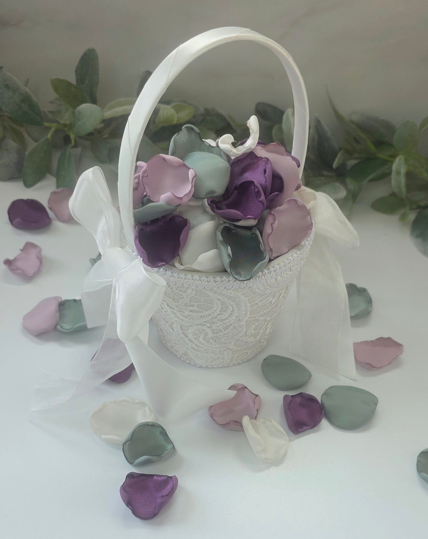 A mix of different shades of purple and sage green rose petals in Ivory flower girl basket. Includes Wisteria, Dusk Purple, Ivory and dusty sage rose petals for flower girl toss, aisle decor, photo flatlays, table scatter. Perfect for future brides planning a classic wedding or Love in Bloom or Whimsical bridal shower event ideas.