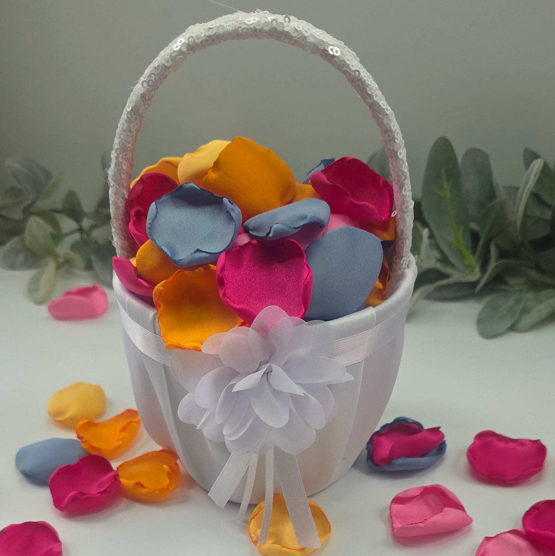 A mix of Tangerine Mango Orange, Fuchsia, Candy pink, sunset orange and dusty blue rose petals in white flower girl baslet. Perfect for aisle decor, flower girl tossing. table scatter, backdrop accents or photo flatlays ideas. A golden hour, topical, and sunset vibes for a future bride planning a wedding ceremony or bridal shower event. A bold colorful, modern color palette inspiration and wedding decor ideas. 