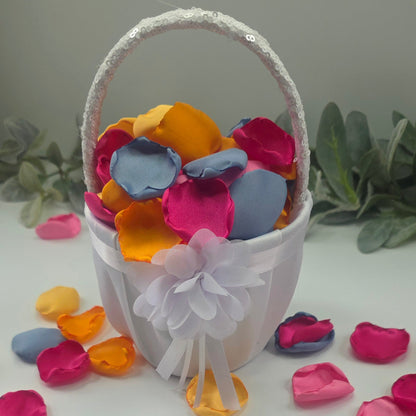 A mix of Tangerine Mango Orange, Fuchsia, Candy pink, sunset orange and dusty blue rose petals in white flower girl baslet. Perfect for aisle decor, flower girl tossing. table scatter, backdrop accents or photo flatlays ideas. A golden hour, topical, and sunset vibes for a future bride planning a wedding ceremony or bridal shower event. A bold colorful, modern color palette inspiration and wedding decor ideas. 